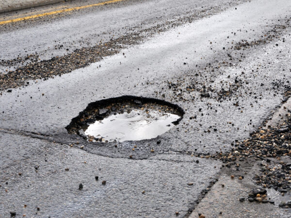 A large pot hole filled with water on an asphalt road A road damaged by rain,snow, or the freeze/thaw cycle that is in need of maintenance.